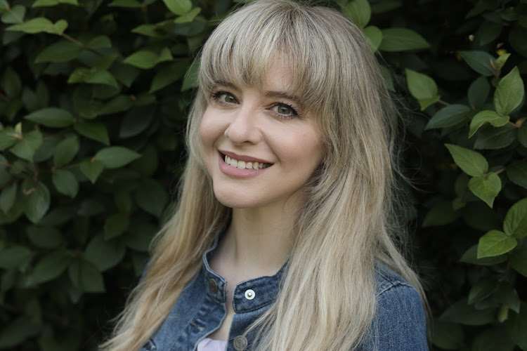 Jenilyn in a denim jacket in front of green leaves