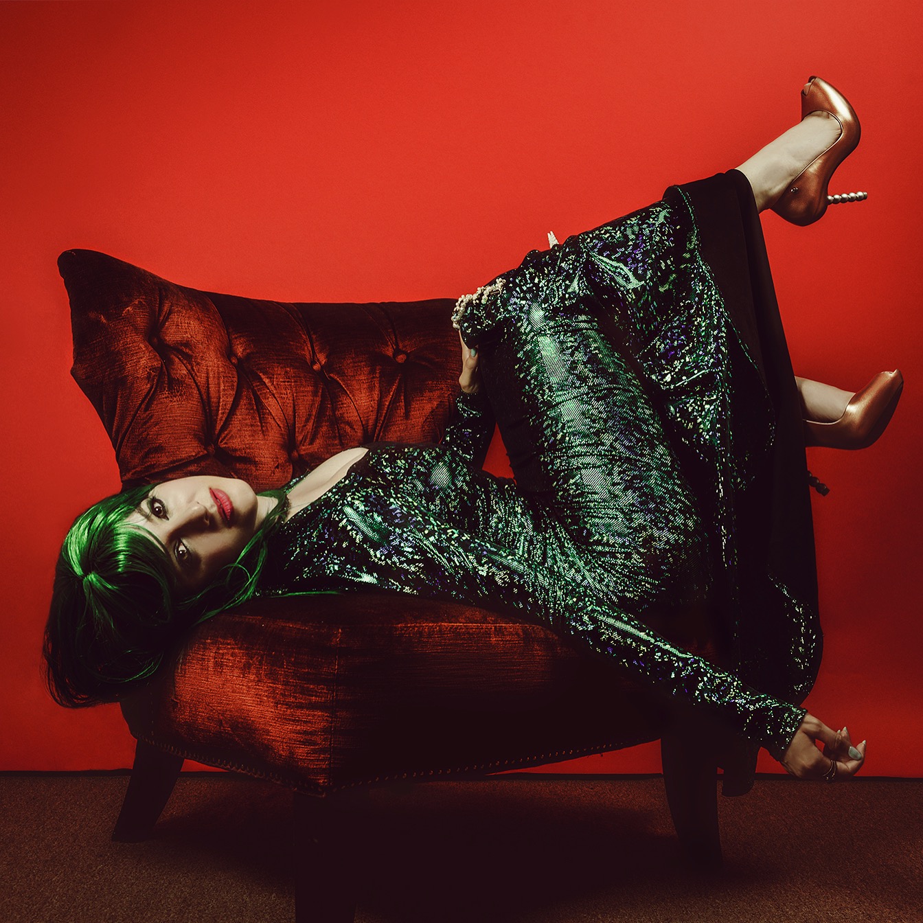 Editorial portrait in an emerald wig and sequins on a red velvet chair